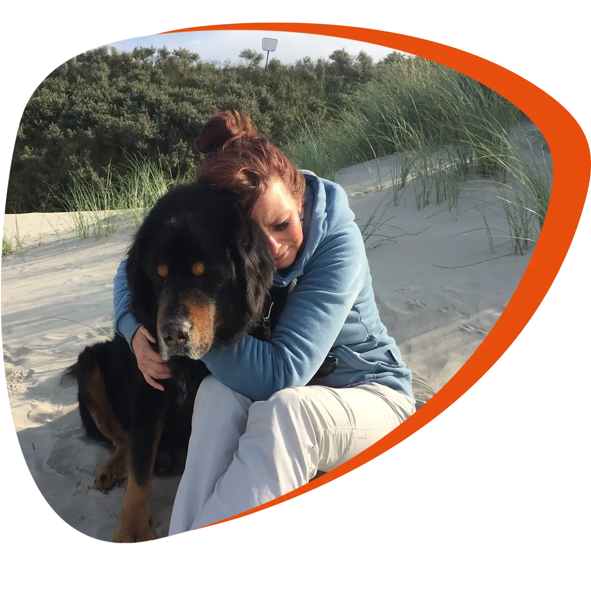 Frau umarmt am Strand sitzend innig ihren Hund